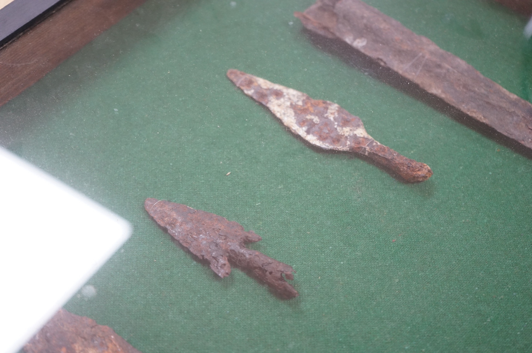 A display cabinet with a collection of antiquities comprising; medieval spur, spear and arrow heads, 53cm high. Condition - fair, relic condition